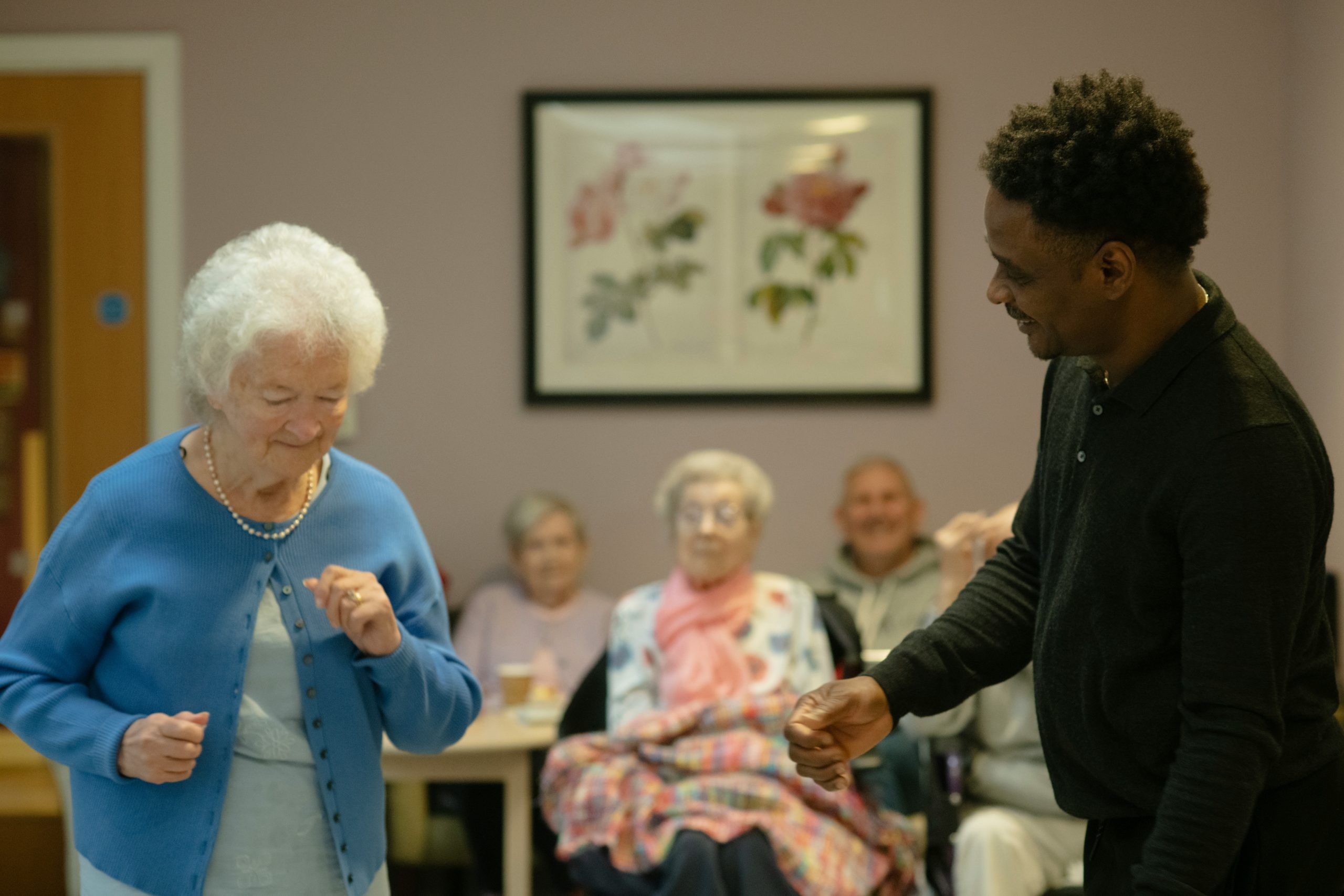Seniorin tanzt gemeinsam mit einem Betreuer in einer Pflegeeinrichtung und zeigt Freude, Bewegung und Aktivierung als Teil der Wohngemeinschaft.
