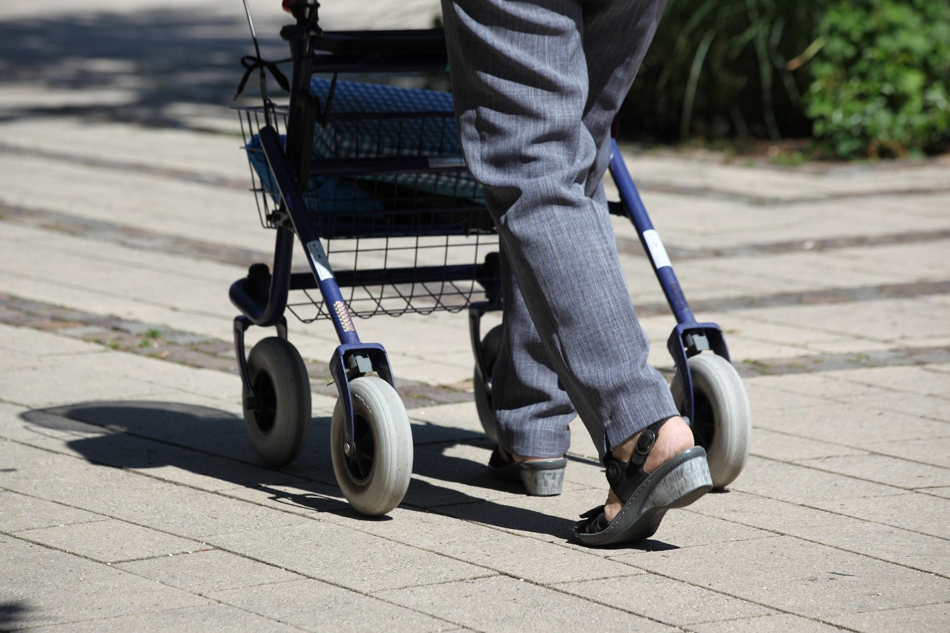 Eine älterePerson geht mit einem Rollator über einen gepflasterten Weg und nutzt die Gehhilfe für mehr Sicherheit und Stabilität im Alltag.